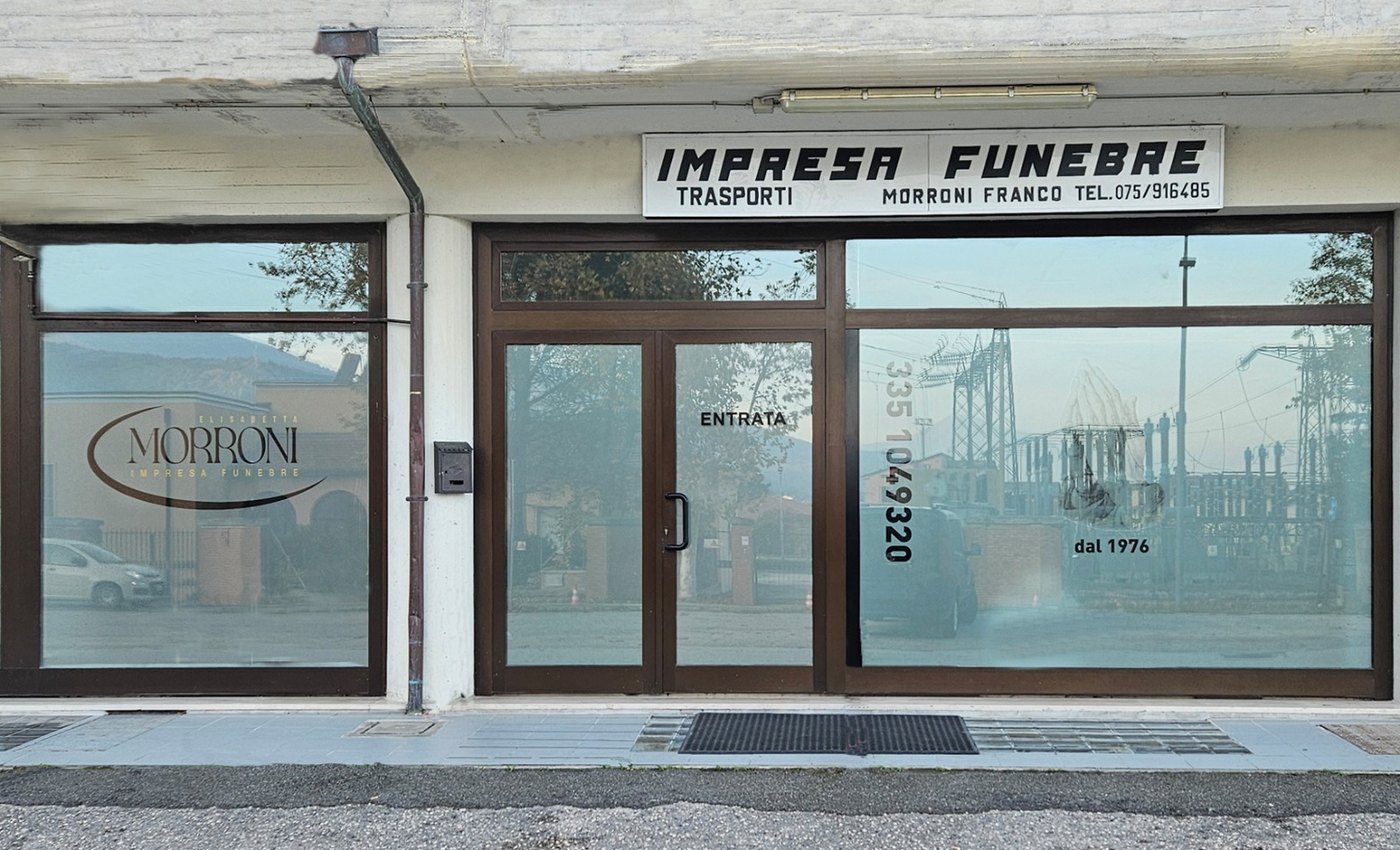 Vetrate con infissi marroni sotto l'insegna «Impresa Funebre Trasporti Morroni Franco» e scritta «dal 1976